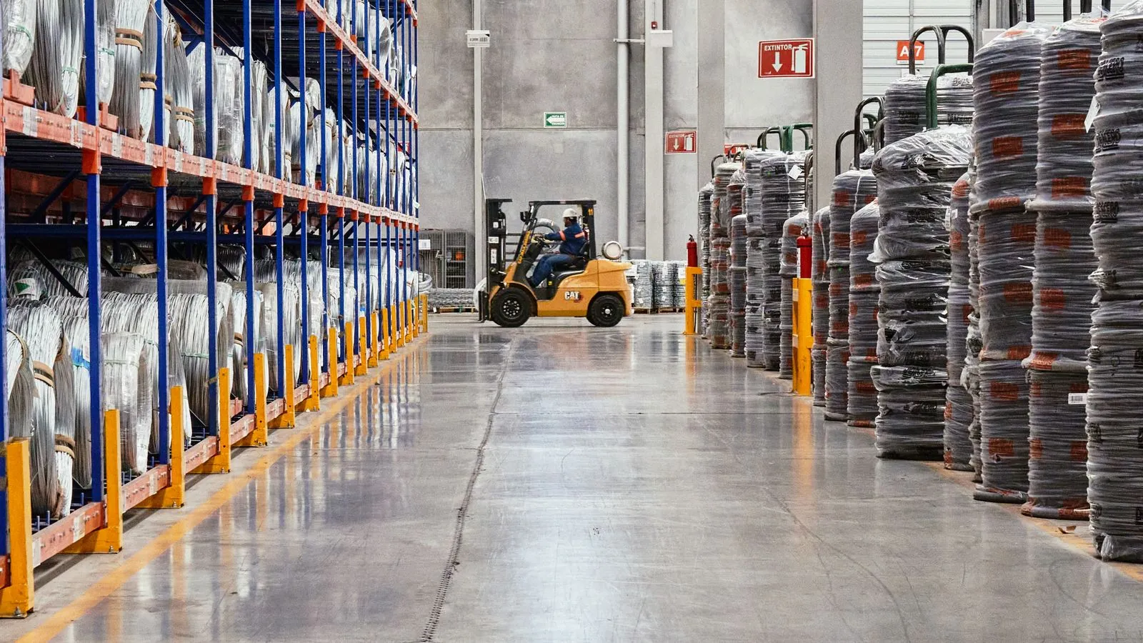 Bodega industrial con estanterías metálicas cargadas de equipos embalados y un montacargas circulando entre los pasillos